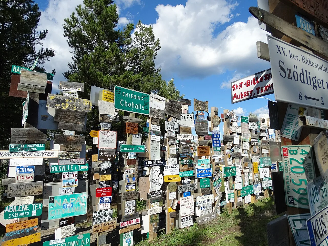 Photographie de la Sign Post Forest à Watson Lake, au Yukon, des centaines de panneaux de villes et de plaques d'immatriculation cloués à des poteaux de bois sous un ciel bleu